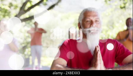 Immagine di macchie di luce e alberi su diverse persone anziane che praticano yoga in giardino Foto Stock