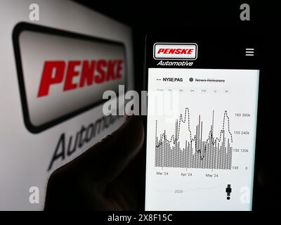 Persona che detiene un cellulare con il sito Web della concessionaria statunitense Penske Automotive Group Inc. Davanti al logo. Messa a fuoco al centro del display del telefono. Foto Stock