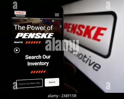 Persona che possiede uno smartphone con pagina Web della concessionaria statunitense Penske Automotive Group Inc. Davanti al logo. Messa a fuoco al centro del display del telefono. Foto Stock