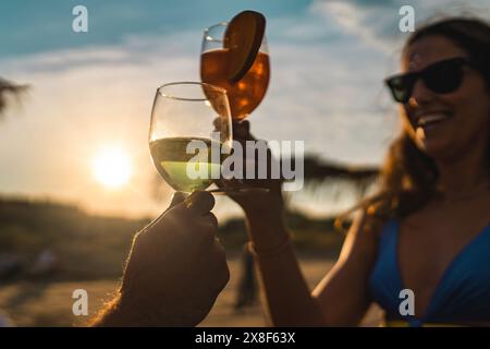 Due persone brindano con bevande al tramonto sulla spiaggia, celebrando i momenti estivi, gustando bevande rinfrescanti, calda luce serale e Beach vib Foto Stock