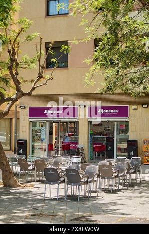 Viladecans, Barcellona, Spagna - 25 maggio 2024: Un angolo di riposo in città, la terrazza del negozio Jijonenca offre uno spazio ombreggiato con sedie e tabl Foto Stock