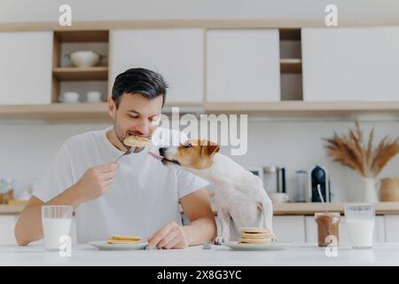 Un uomo che condivide un momento tenero con il suo cane, desideroso di un boccone di pancake a colazione. Foto Stock