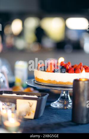 Torta al formaggio con mirtilli e fragole sul tavolo con tovaglia blu per festeggiare il compleanno Foto Stock