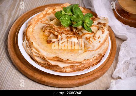 Crepe sottili fatte in casa (pancake) con miele impilato in una pila, su un tavolo con latte e uova in un cestino. Cibo in stile country. Slavonia tradizionale, pennsylvania Foto Stock