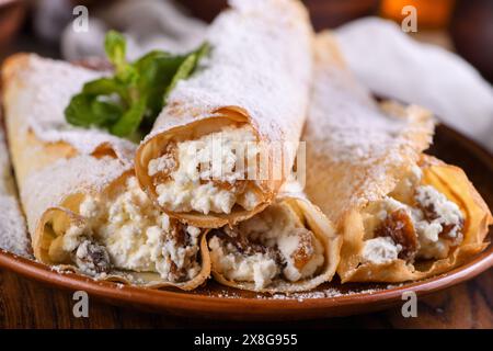 Pancake sottili ripieni di formaggio cottage, miele e uva passa, arrotolati sotto forma di tubetto, cosparsi di zucchero in polvere, guarniti con menta. Festivo Foto Stock