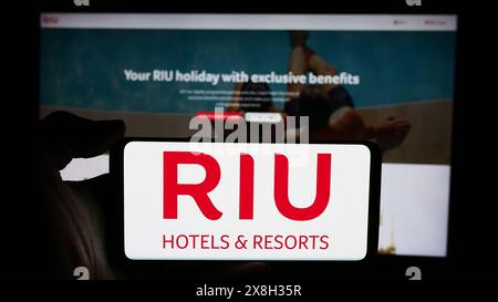 Persona che detiene un cellulare con il logo della società alberghiera spagnola RIU Hotels and Resorts di fronte alla pagina web aziendale. Mettere a fuoco il display del telefono. Foto Stock