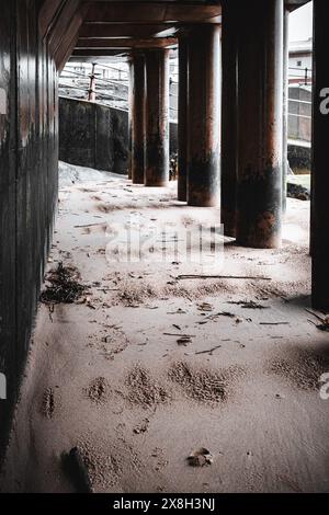 Tranquillo passaggio pedonale sotto il ponte urbano con colonne di cemento e pavimento di sabbia, creando un'atmosfera tranquilla e quasi abbandonata Foto Stock