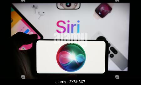 Persona che detiene un cellulare con il logo del software di assistente digitale Siri (Apple Inc.) davanti alla pagina Web aziendale. Mettere a fuoco il display del telefono. Foto Stock