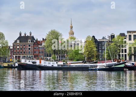 Paesi Bassi, Amsterdam - 7 aprile 2024: Città vecchia con case tradizionali olandesi, chiatte e case galleggianti, paesaggio urbano lungo la banchina di Oosterdok Foto Stock