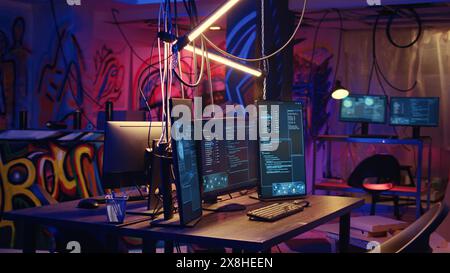 Panning di un sistema informatico ad alta tecnologia che esegue codice dannoso in cantina vuoto. Il PC monitora in un nascondiglio criminale vuoto illuminato al neon utilizzato dagli hacker per commettere attività illegali Foto Stock