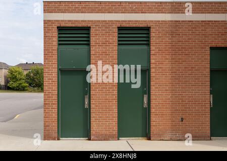 Tre porte verdi - adagiate su pareti di mattoni rossi adiacenti al parcheggio vuoto - case e alberi distanti sotto il cielo nuvoloso. Presa a Toronto, Canada. Foto Stock