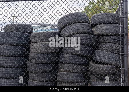 Pneumatici usati impilati in alto - visibili attraverso la recinzione a maglie a catena - sotto il cielo coperto grigio. Presa a Toronto, Canada. Foto Stock