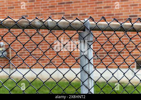 Vista ravvicinata - recinzione a catena - palo metallico resistente agli agenti atmosferici - sfondo della parete in mattoni arancioni. Presa a Toronto, Canada. Foto Stock