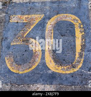 Il numero 30 in giallo su una parete di cemento Foto Stock