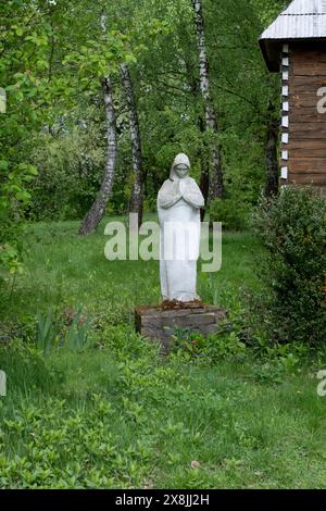 Una vecchia statua della madre di Dio, danneggiata, abbandonata nel Cimitero, alberi sfocati con foglie verdi sullo sfondo. Foto Stock