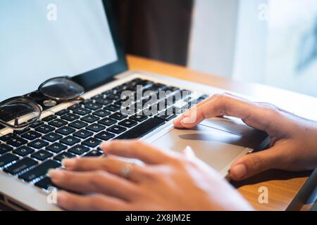 Primo piano della digitazione delle mani sulla tastiera di un notebook con gli occhiali posizionati lateralmente. Foto Stock