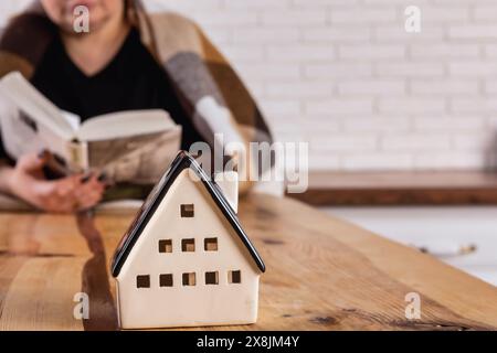 accogliente soggiorno con un piccolo modello della casa bianca sul tavolo. In questo ambiente caldo e accogliente, una donna è seduta a un tavolo a leggere un b Foto Stock