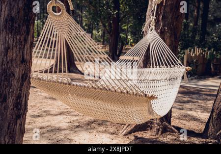 Un'amaca bianca di corda oscilla tra due alberi Foto Stock