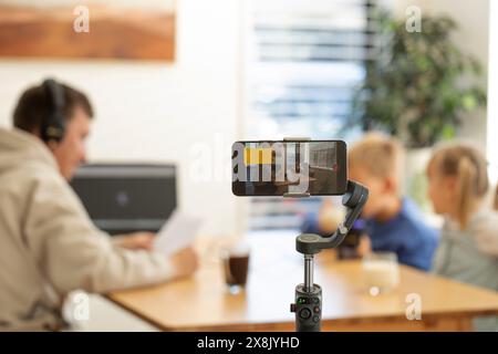 Una famiglia registra un podcast a casa, utilizzando uno smartphone e una configurazione del microfono con un bambino che partecipa Foto Stock