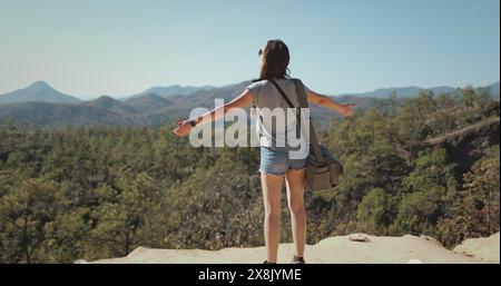 Una donna è in piedi sulla cima di una montagna in Thailandia, braccia allungate. Le riprese al rallentatore catturano la sua posizione trionfale sullo sfondo mozzafiato delle montagne. Foto Stock