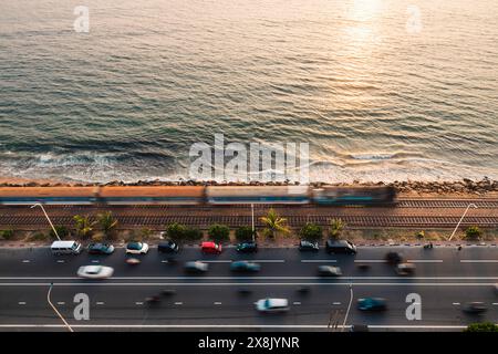 Strada e ferrovia lungo la costa al tramonto sull'oceano Indiano. Treno in arrivo a Colombo, Sri Lanka. Foto Stock