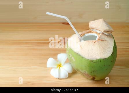 Succo di cocco naturale fresco in guscio di cocco con fiore di Frangipani isolato su un tavolo di legno Foto Stock
