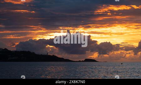 Tramonto incandescente dietro il faro, cielo con nuvole illuminate dal sole sopra un faro sulla costa del nord della Spagna, arancione e colori scuri di Foto Stock