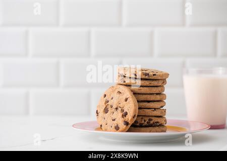 I biscotti vengono spalmati su un piatto, un bicchiere di latte fresco. Biscotti fatti in casa con gocce di cioccolato. Foto Stock
