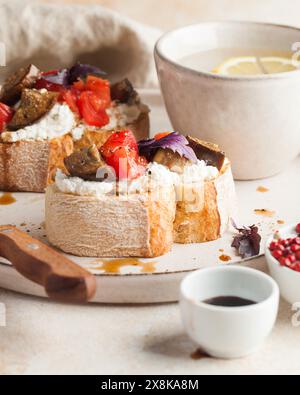 Deliziosa bruschetta condita con formaggio morbido, fette di pomodoro fresco e melanzane arrosto. Foto Stock