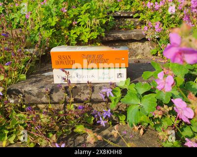 Stack of Books di autori britannici in a Spring Flowers Garden The Rich Are Different Novel di Susan Howatch e Past Mischief di Victoria Clayton Foto Stock