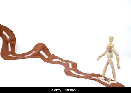 Manichino di legno che cammina su una strada ondulata in pelle marrone, viaggia verso un concetto di obiettivo, ravvicinato isolato Foto Stock
