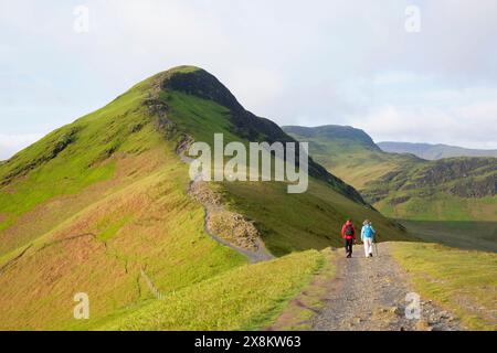 Lake District National Park, Cumbria, Inghilterra. Due escursionisti che camminano verso la cima di Cat Bells da Skelgill Bank, all'alba. Foto Stock