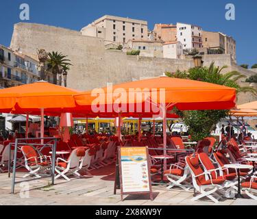 Calvi, Haute-Corse, Corsica, Francia. Colorato caffè con pavimentazione sul porto in Quai Landry sotto le massicce mura della cittadella genovese. Foto Stock