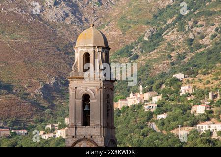 Feliceto, Haute-Corse, Corsica, Francia. Imponente campanile della seicentesca Église Saint-Nicolas, il vicino villaggio di Nessa oltre. Foto Stock
