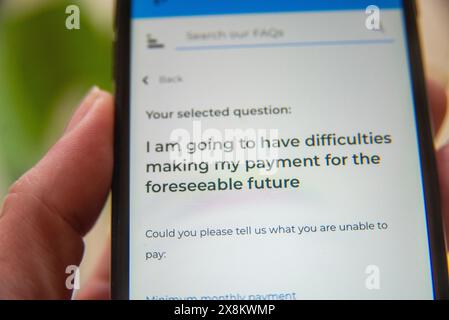 Mano con un telefono cellulare che visualizza una pagina di domande frequenti sulle future difficoltà di pagamento, concentrandosi sull'assistenza finanziaria e sulle opzioni di supporto. Foto Stock