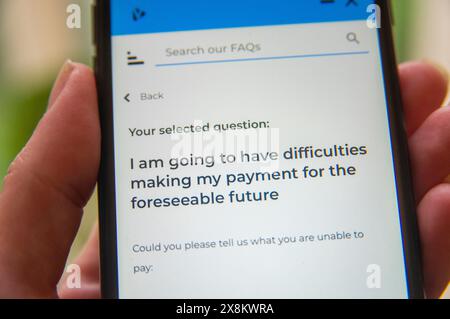 Mano con un telefono cellulare che visualizza una pagina di domande frequenti sulle future difficoltà di pagamento, concentrandosi sull'assistenza finanziaria e sulle opzioni di supporto. Foto Stock