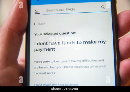 Mano con un telefono cellulare che visualizza una pagina di domande frequenti sulle future difficoltà di pagamento, concentrandosi sull'assistenza finanziaria e sulle opzioni di supporto. Foto Stock