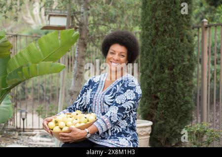 Donna afroamericana che tiene in mano una ciotola di guava coltivate in un giardino californiano. Foto Stock