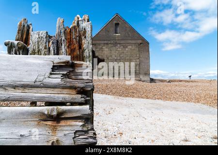 Abbandonata la Mary Stanford Lifeboat Station in cemento grigio, la riserva naturale di Rye Harbour, una giornata di sole con un cielo blu intenso e difese marittime danneggiate Foto Stock