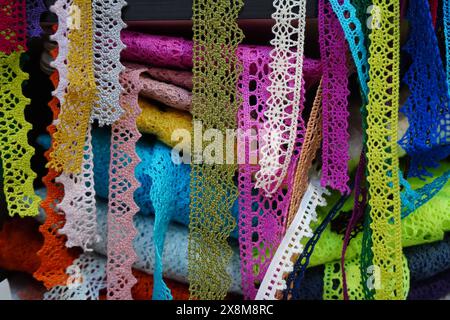 Nastri in pizzo in diversi colori e motivi appesi ai rotoli sullo scaffale del negozio di merceria. Elementi decorativi da cucire sugli indumenti. Foto Stock