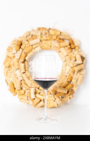 Un bicchiere di vino rosso su una tavola bianca, sullo sfondo di una corona di sugheri. Messa a fuoco selezionata. Foto di alta qualità Foto Stock