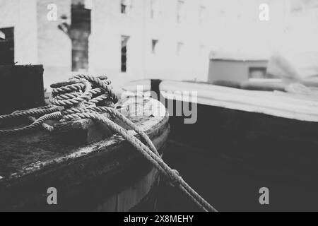 Immagine in bianco e nero della barca attraccata con corde annodate dettagliate e dintorni industriali, che evocano un'atmosfera rustica e nautica. Castlefield Manchester Regno Unito Foto Stock