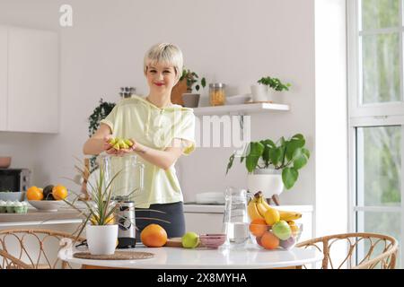 Giovane donna sportiva che mette la mela tagliata nel frullatore in cucina Foto Stock