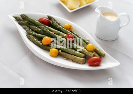 Fonte di grande fibra alimentare, asparagi verdi cotti al forno serviti in un piatto bianco, preparato come contorno con pomodori colorati Foto Stock