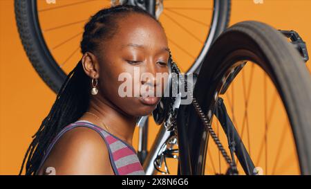 Primo piano del meccanico che spinge i pedali per far girare la ruota della bici, esaminandola dopo aver modificato e lubrificato le parti. Il dipendente sta ascoltando eventuali segni di stridio negli anelli delle catene delle biciclette rumorosi, la telecamera A. Foto Stock