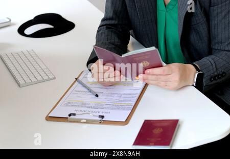 Vista dall'alto di una donna che compila i documenti per la richiesta di visto con un passaporto tedesco su un tavolo dell'ufficio Foto Stock