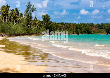 Piccole barche da pesca ancorate al largo di una piccola spiaggia tropicale circondata da palme in Thailandia Foto Stock