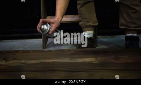 Uomo che dipinge travi di legno, primo piano. Supporto. Uomo lavoratore che utilizza vernice spray nera per verniciare il tronco. Foto Stock
