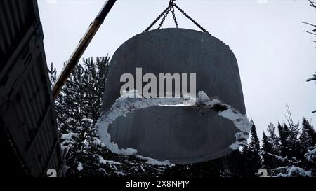 Visuale ad angolo basso della gru che trasporta dettagli in calcestruzzo in cantiere contro il cielo. Fermo. Lavori industriali e alberi invernali. Foto Stock