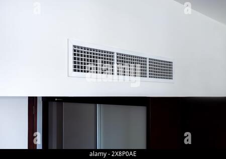 Vista laterale del sistema di ventilazione a parete dell'aria condizionata sul soffitto nelle camere bianche e nere dell'hotel. Griglia di ventilazione dell'aria in camera Foto Stock